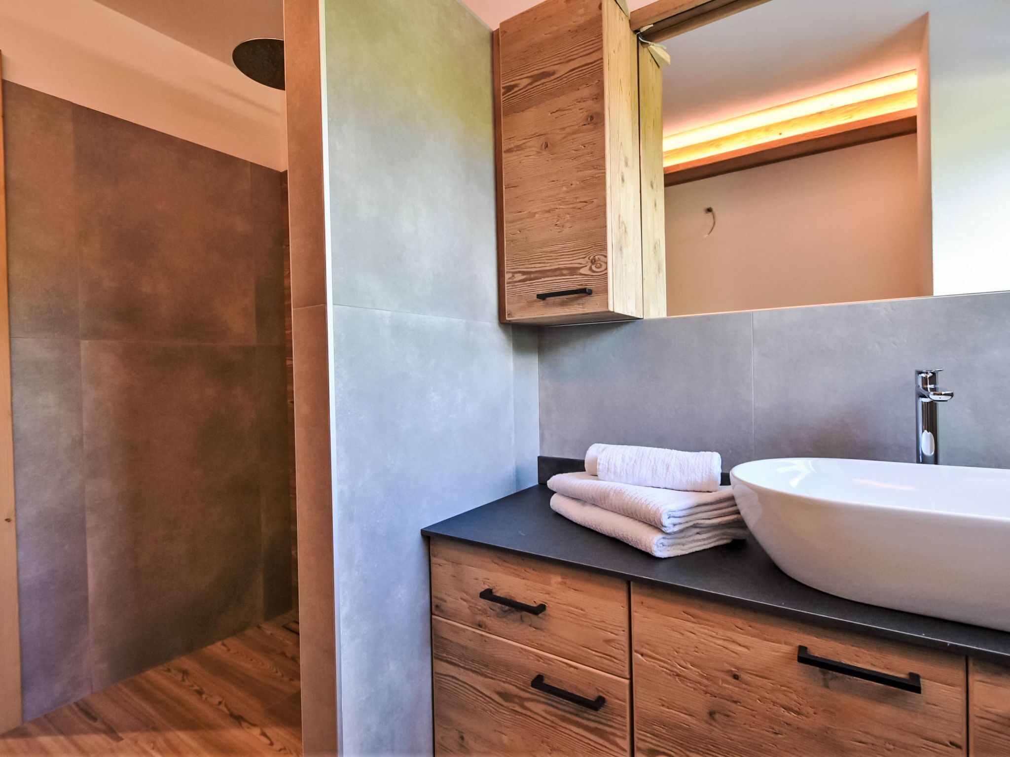 Ein modernes Badezimmer mit einem großen Waschbecken, Holzschränken und einem Spiegel.