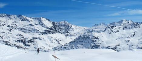 A snowy mountain landscape with a clear sky and a single skier in the distance.