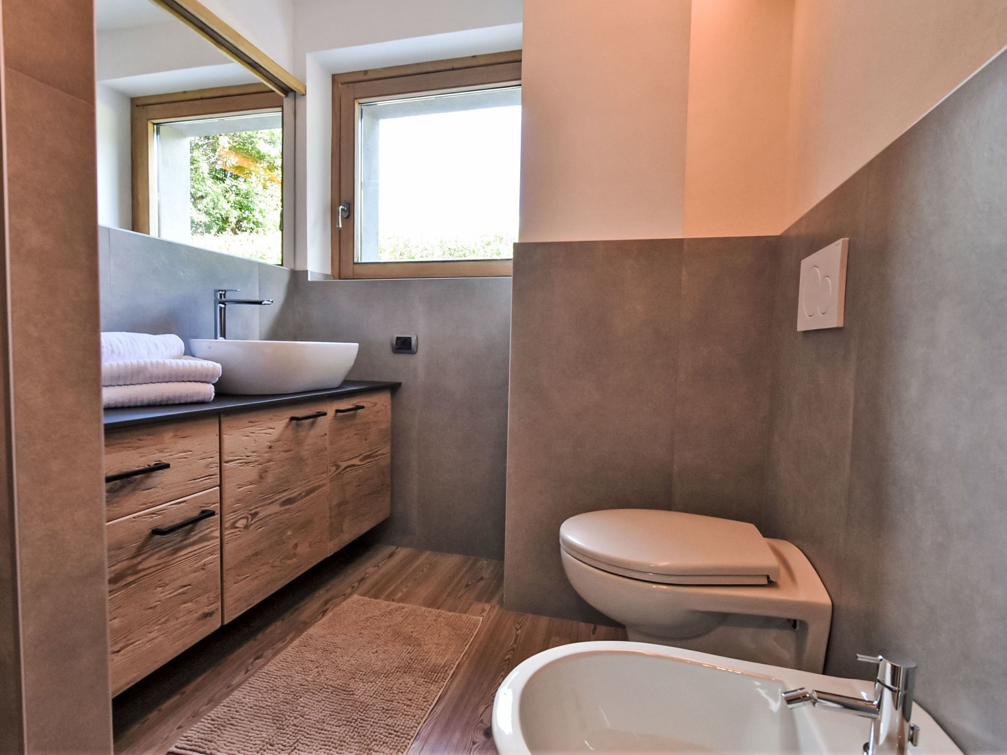 A modern bathroom with a wooden vanity, a vessel sink, a toilet, and a freestanding bathtub.