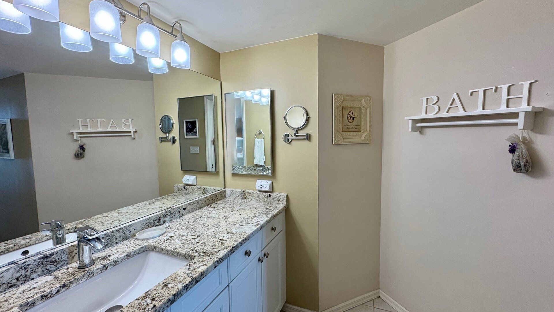 A bathroom with a granite countertop sink, two mirrors, a vanity, and a 'BATH' sign on the wall.