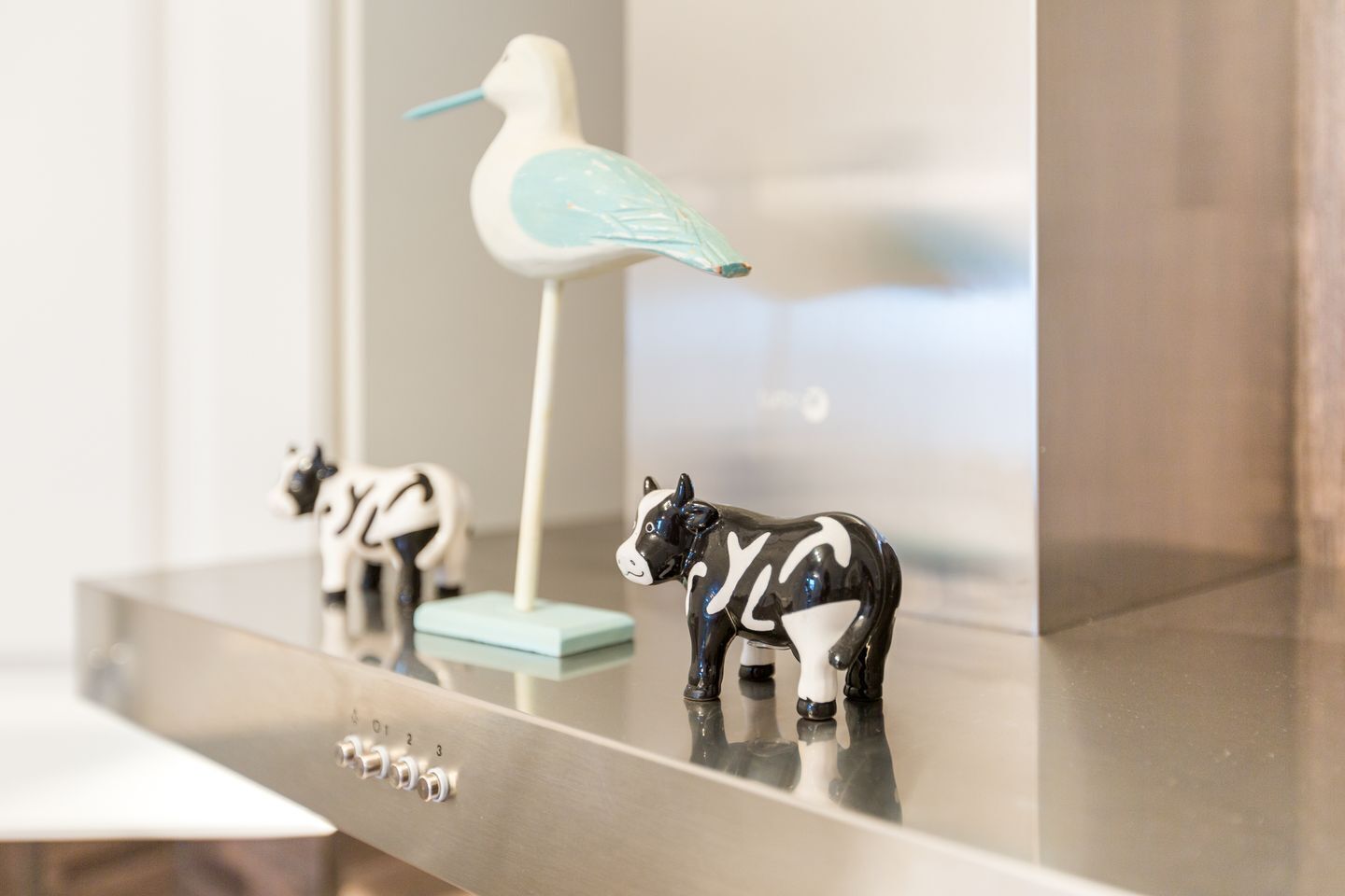 A modern kitchen with a stainless steel countertop, a white bird figurine, and a cow figurine.