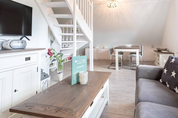 A modern living room with a wooden coffee table, a grey sofa, a TV, and a staircase leading to another level.