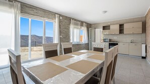 Eine moderne Küche mit eingebauten Geräten, ein Essbereich mit Tisch und Stühlen sowie große Fenster mit Blick ins Freie.