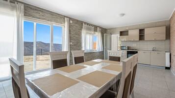 A modern kitchen with built-in appliances, a dining area with a table and chairs, and large windows offering a view of the outdoors.