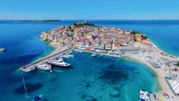 An aerial view of a coastal town with a marina, clear blue waters, and a prominent church on a hill.