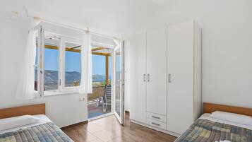 A bedroom with two beds, a wardrobe, and a balcony with a view.