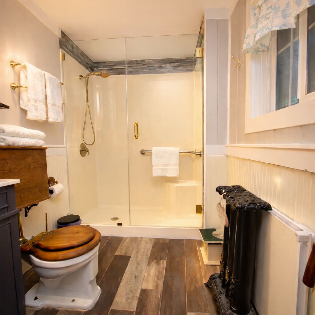 A bathroom with a wooden toilet, a glass-enclosed shower, and a radiator.