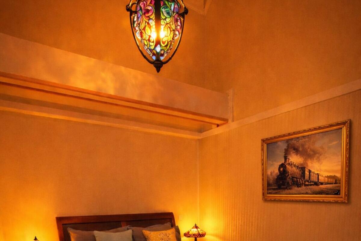 Ein Schlafzimmer mit einem hölzernen Bett, zwei Nachttischen mit Lampen, einem Gemälde an der Wand und einer schrägen Decke.