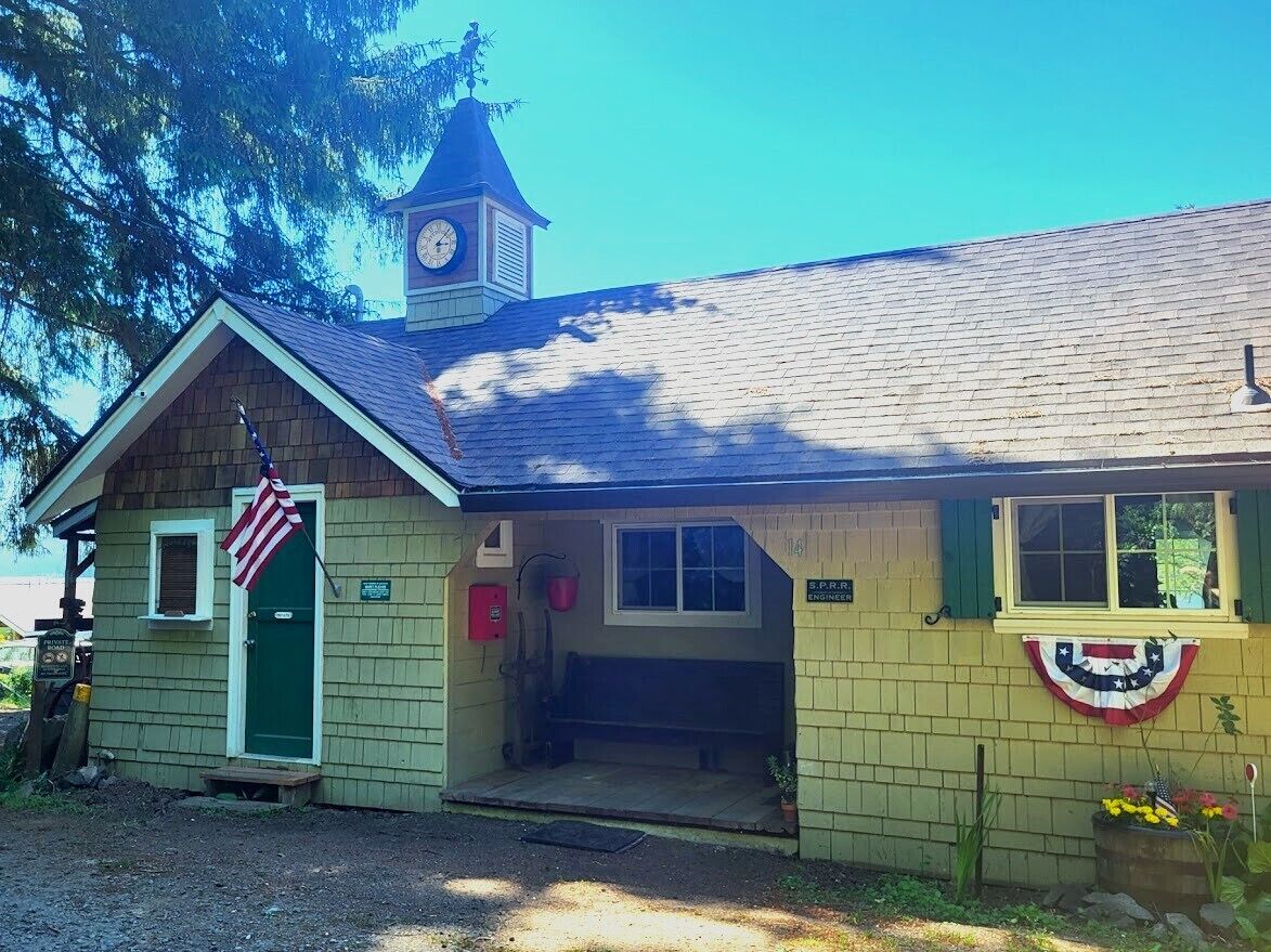 A small building with a clock tower, a green door, and a bench outside.