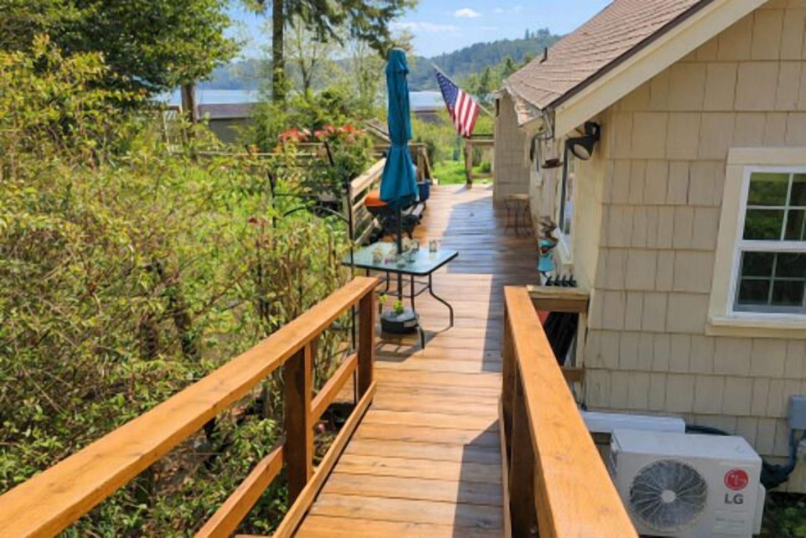 Un patio di legno conduce a una casa, con una bandiera americana, un tavolo con sedie e un condizionatore d'aria.