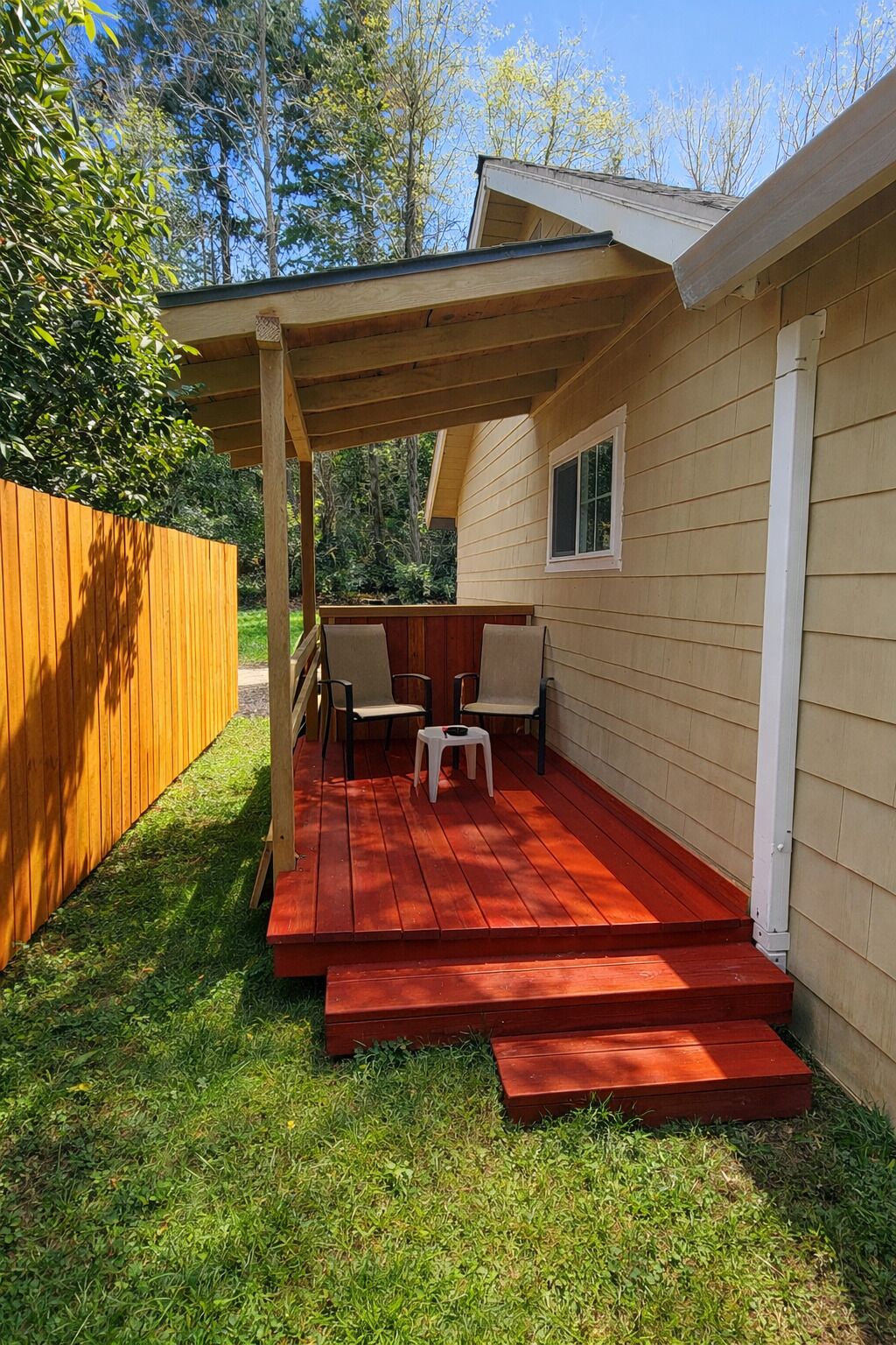 Un patio couvert avec une terrasse en bois, une petite table, deux chaises et une fenêtre.