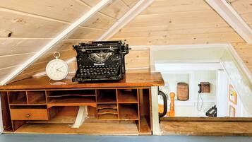 A wooden desk with a typewriter and a clock in a room with wooden walls and a sloped ceiling.