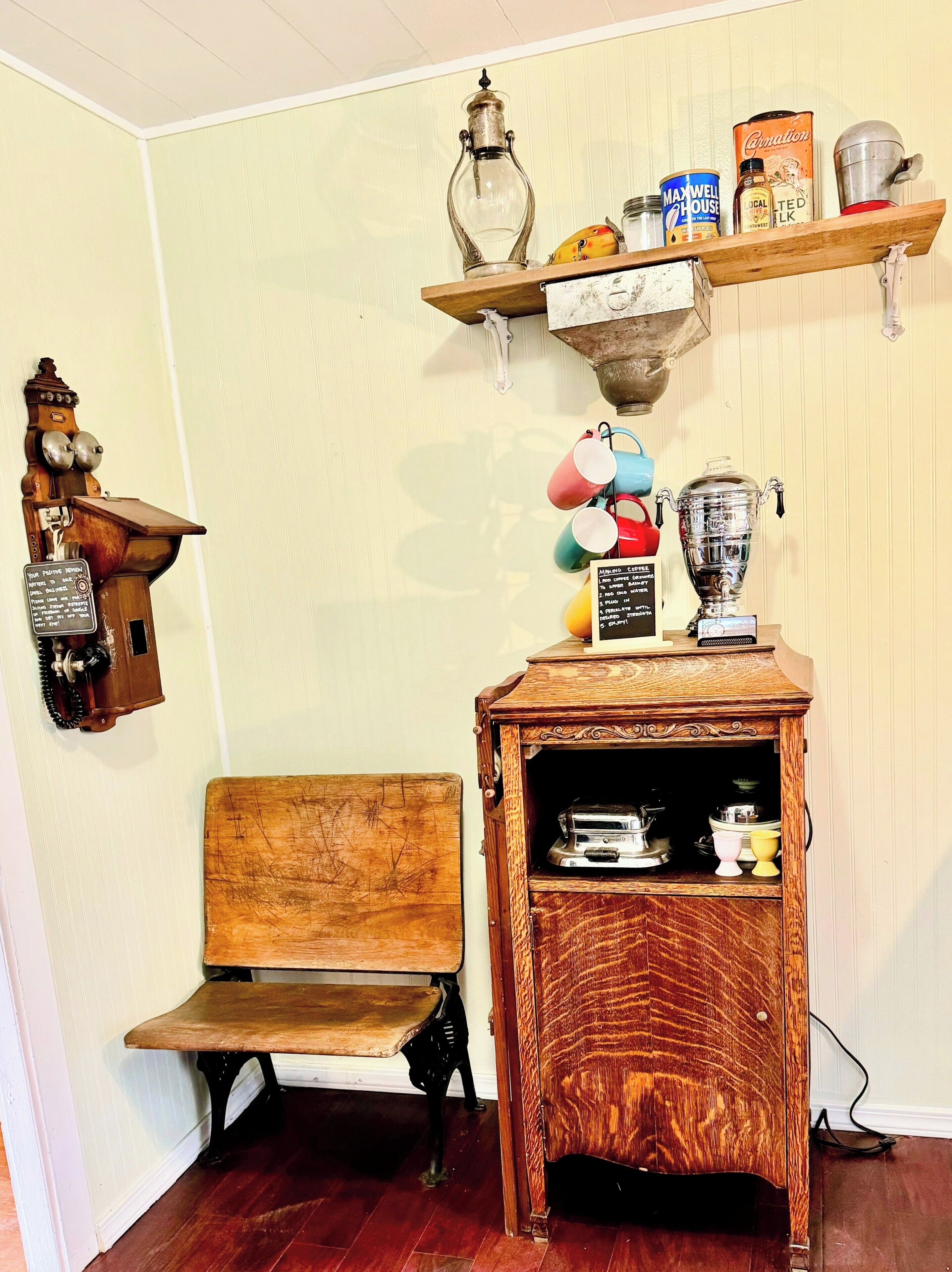 A vintage coffee machine, a wooden bench, and a shelf with various items including a can of Maxwell House coffee and a metal pitcher.