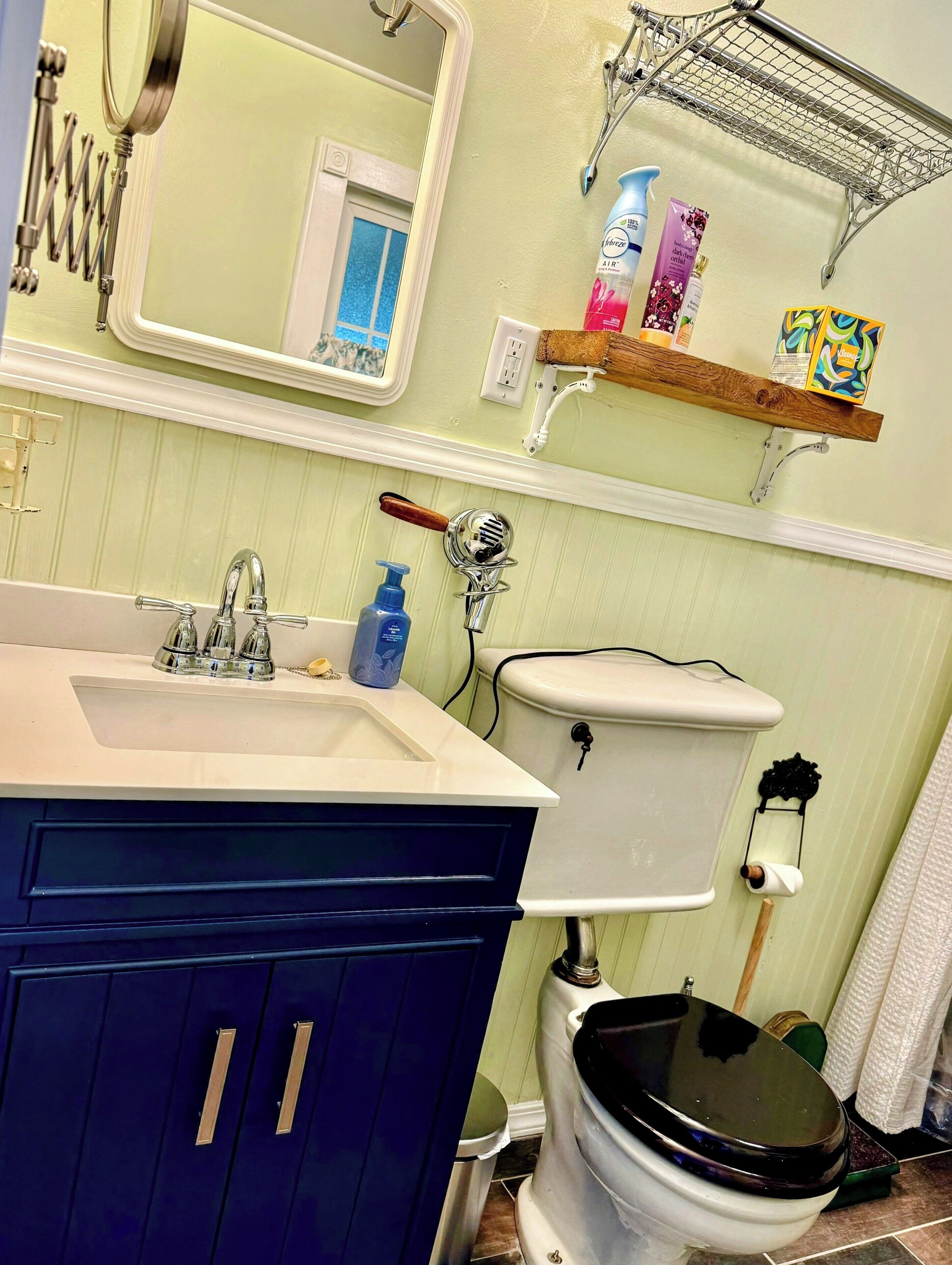 Une salle de bain avec un lavabo blanc, un meuble bleu et des toilettes. On trouve des articles de toilette sur une étagère et un miroir au-dessus du lavabo.