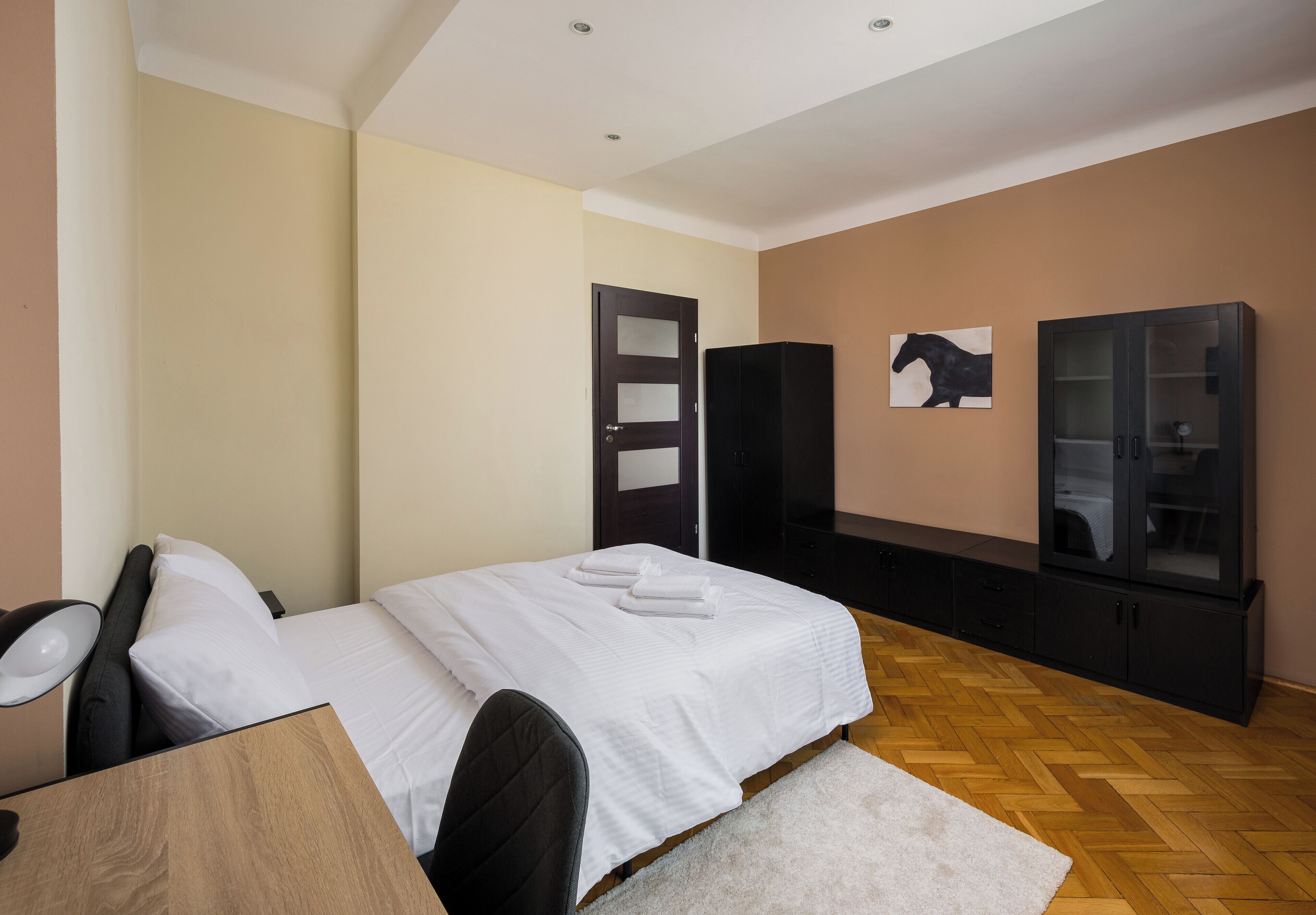 A bedroom with a bed, a desk, a chair, a wardrobe, and a painting on the wall.