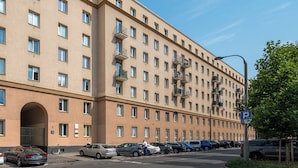A multi-story hotel with a uniform facade, multiple balconies, and a parking area in front.