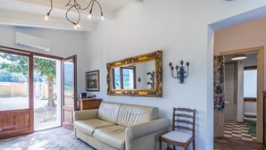 A spacious living room with a beige leather sofa, a wooden chair, a large ornate mirror, and a chandelier. - Casaletto Anticaluce by Interhome (Pastina)