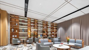 A modern lounge area with seating, a marble-patterned floor, and a wall of shelves with various items. - Platinum International Apartments (Huiyang High speed Railway Station Xinghe COCO Store) (Huizhou)
