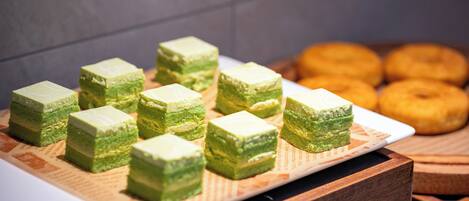 A tray of green layered cakes on a white plate, with a wooden table and a blurred background.