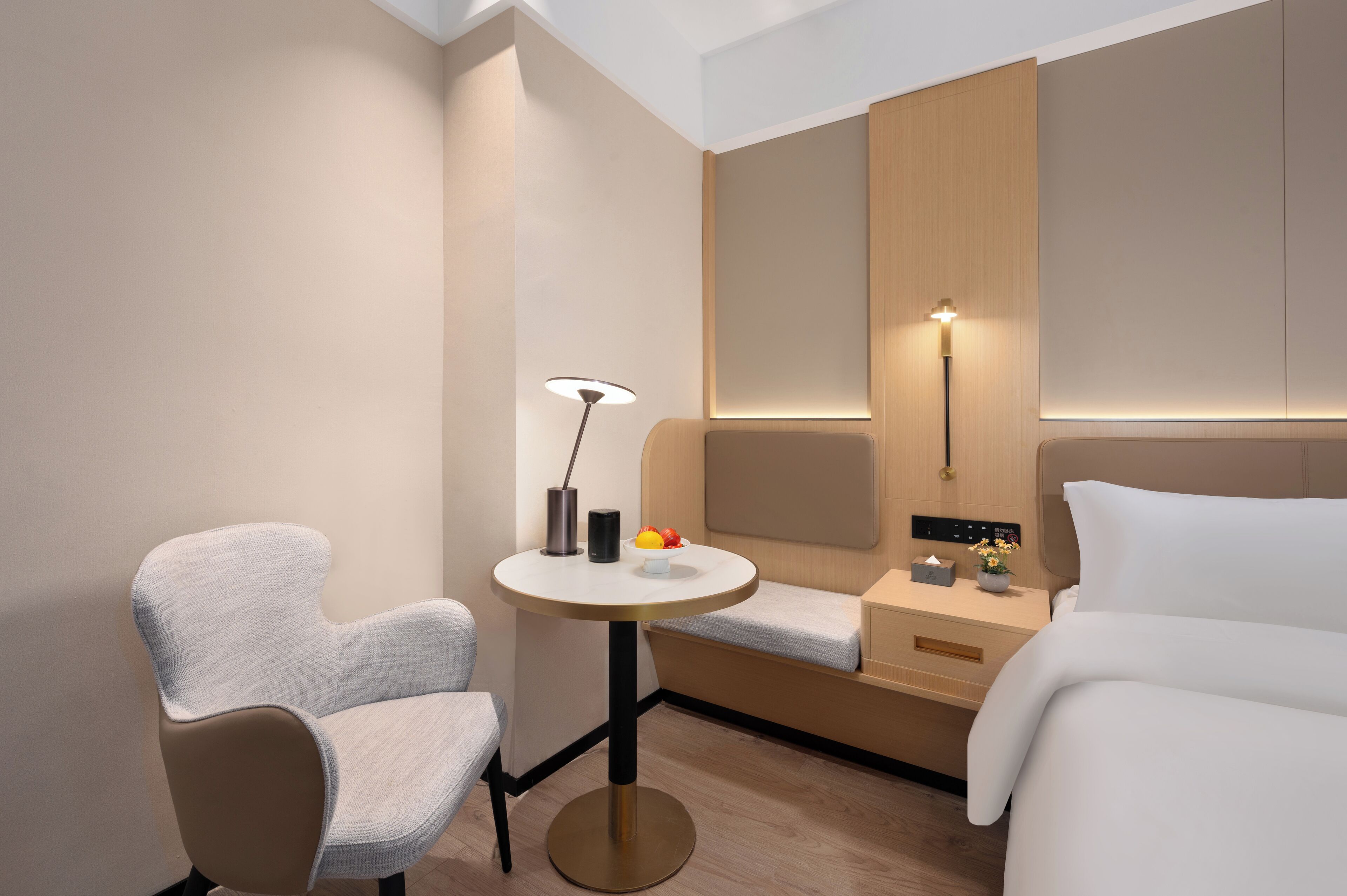 Habitación de hotel moderna con una cama, una silla, una mesita redonda con una lámpara y una mesita de noche con una lámpara y un frutero.