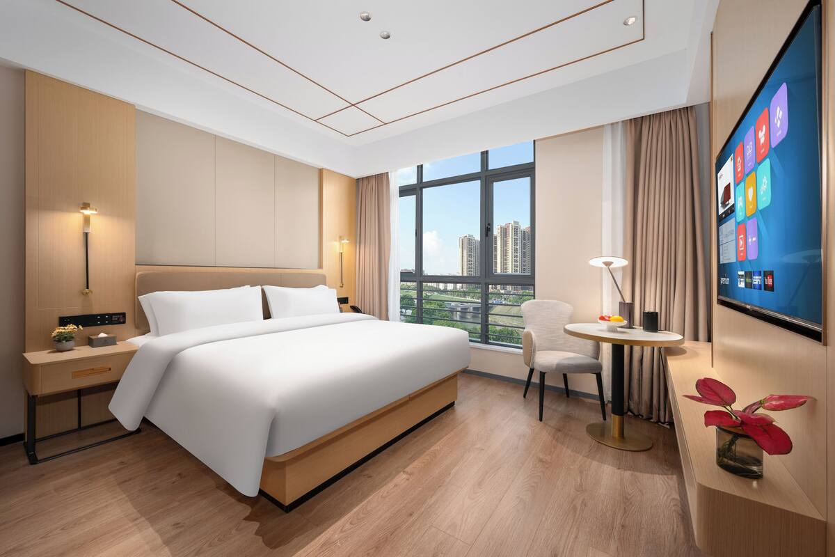 Una habitación de hotel moderna con una cama grande, un escritorio, una silla, un televisor y una ventana con vistas a la ciudad.