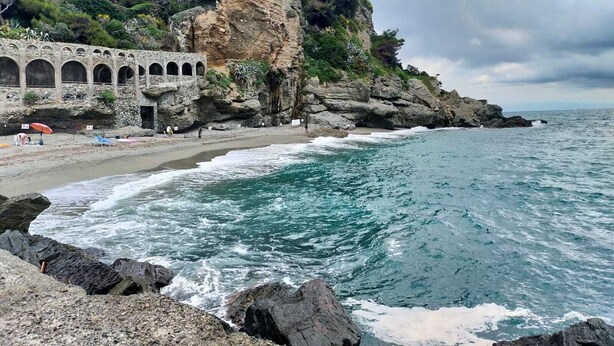 A coastal beach with a rocky cliff and a stone building with arches. - A 7 MIN A PIEDI DAL MARE, 5 DAL CENTRO, ZONA TRANQUILLA E POSTO AUTO PRIVATO (albisola superiore)
