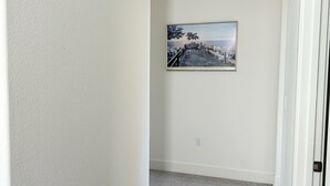 A hallway with a carpeted floor, white walls, and a framed picture on the wall.