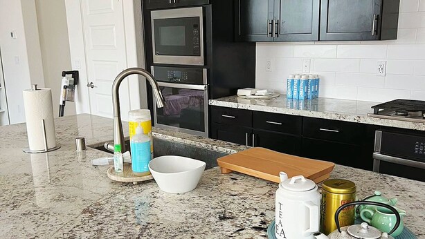 A kitchen with dark cabinets, a granite countertop, a microwave, a stove, and a sink.