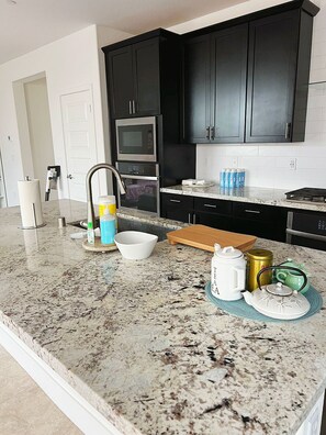 Een keuken met donkere kastjes, een granieten aanrecht, een magnetron, een fornuis en een spoelbak.