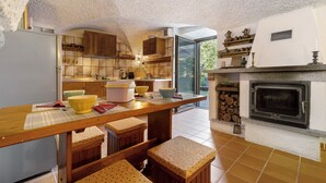 Una cocina con mesa de madera, taburetes, refrigerador y chimenea.