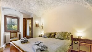 Un dormitorio con una cama grande, una ventana con vistas, un radiador y una mesita de noche con lámpara.