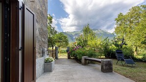Un camino de piedra que conduce a una puerta, un banco y una silla en un jardín con montañas al fondo.