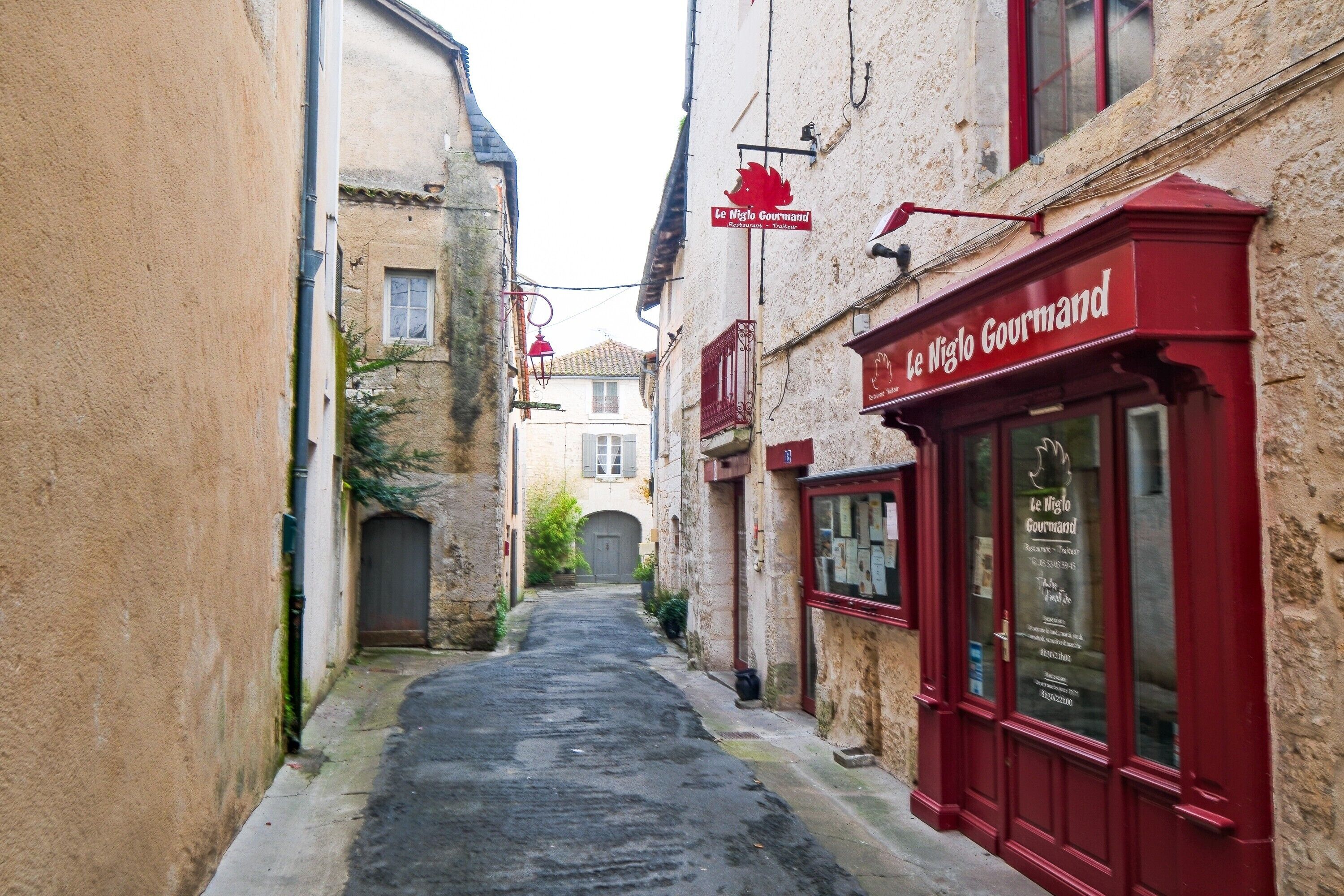 A narrow street with a building on the right labeled 'Le Miglio Gourmand.'