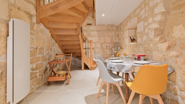 A dining area with a stone wall, wooden staircase, and a table set for four. - Authentic Charm in the Heart of Brantôme’s Historic Center (Brantôme en Périgord)
