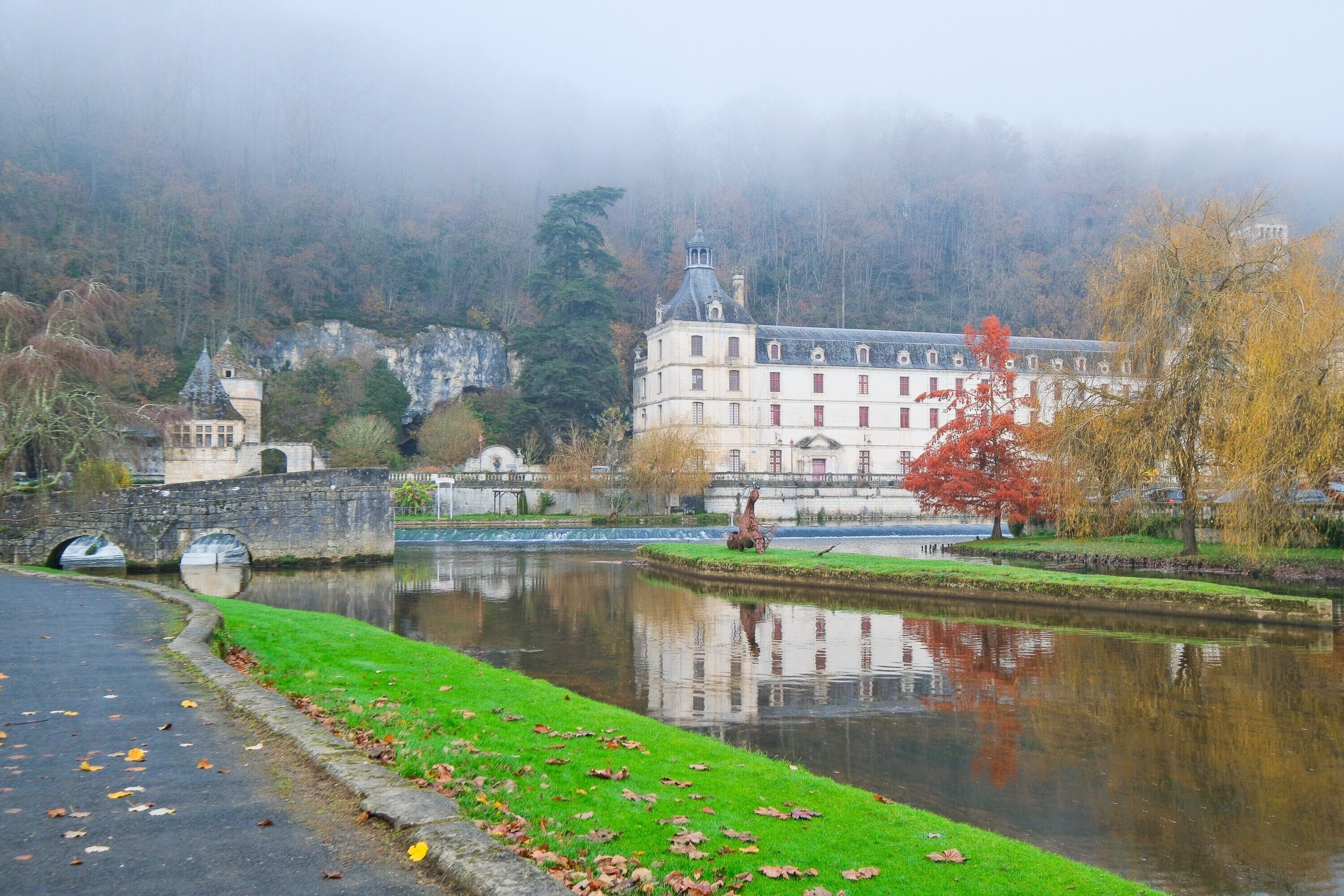 A historic building with a moat, stone bridge, and a statue.