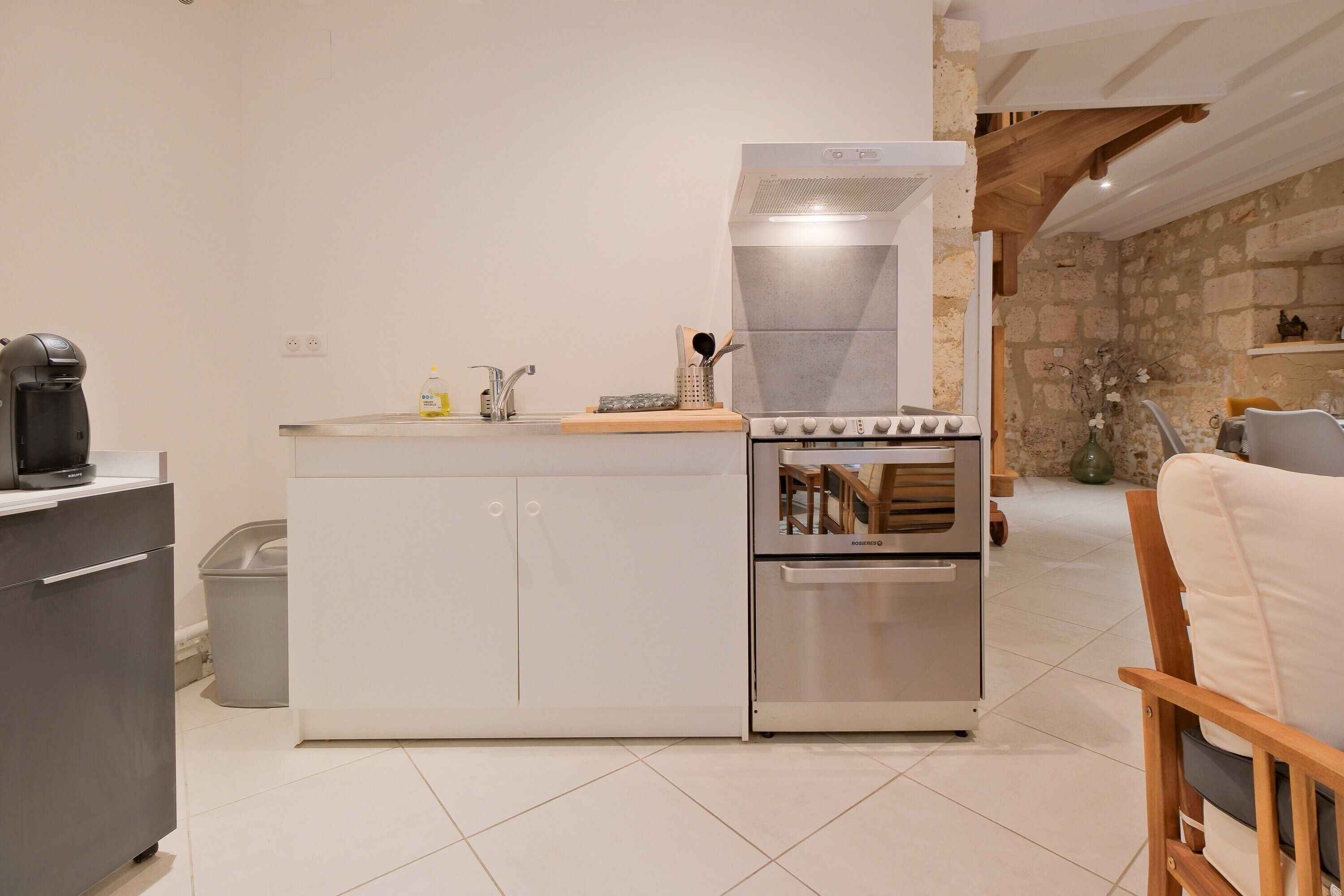 A compact kitchen with a built-in oven, a coffee machine, and a trash bin.