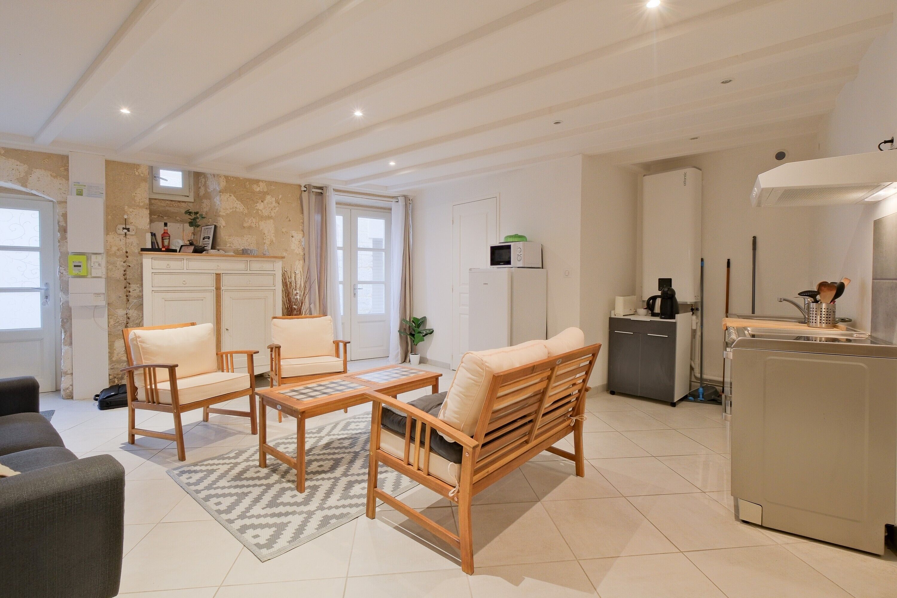 Un salon moderne comprenant un canapé, des fauteuils, une table basse et un coin cuisine avec un réfrigérateur, un four à micro-ondes et un évier.