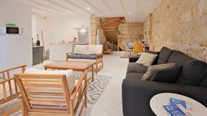 A living room with a sofa, chairs, a coffee table, a kitchen area with a stove and microwave, and a staircase leading to an upper level. - Authentic Charm in the Heart of Brantôme’s Historic Center (Brantôme en Périgord)