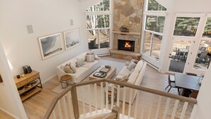 A spacious living room with a stone fireplace, large windows, and a cozy seating area. - Luxury Home - Walk to Arrow Bahn Lift - 6-Bedrooms with 4 Kings & Game Room (Edwards)