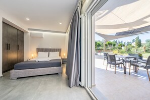 Une chambre à coucher comprenant un lit, une armoire et donnant sur une terrasse extérieure avec des chaises et des tables.