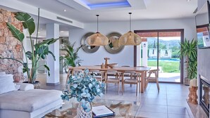 Una sala de estar moderna con sofá, mesa de comedor y sillas, una planta grande y vistas al exterior.