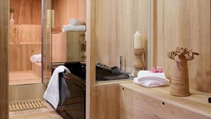 Un sauna de madera con un panel de vidrio, un banco, un perchero para toallas y un jarrón decorativo.