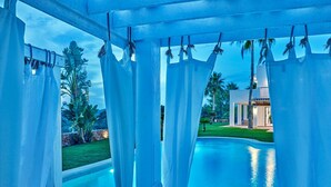 Zona junto a la piscina con vista a un edificio moderno, cortinas y cielo despejado.