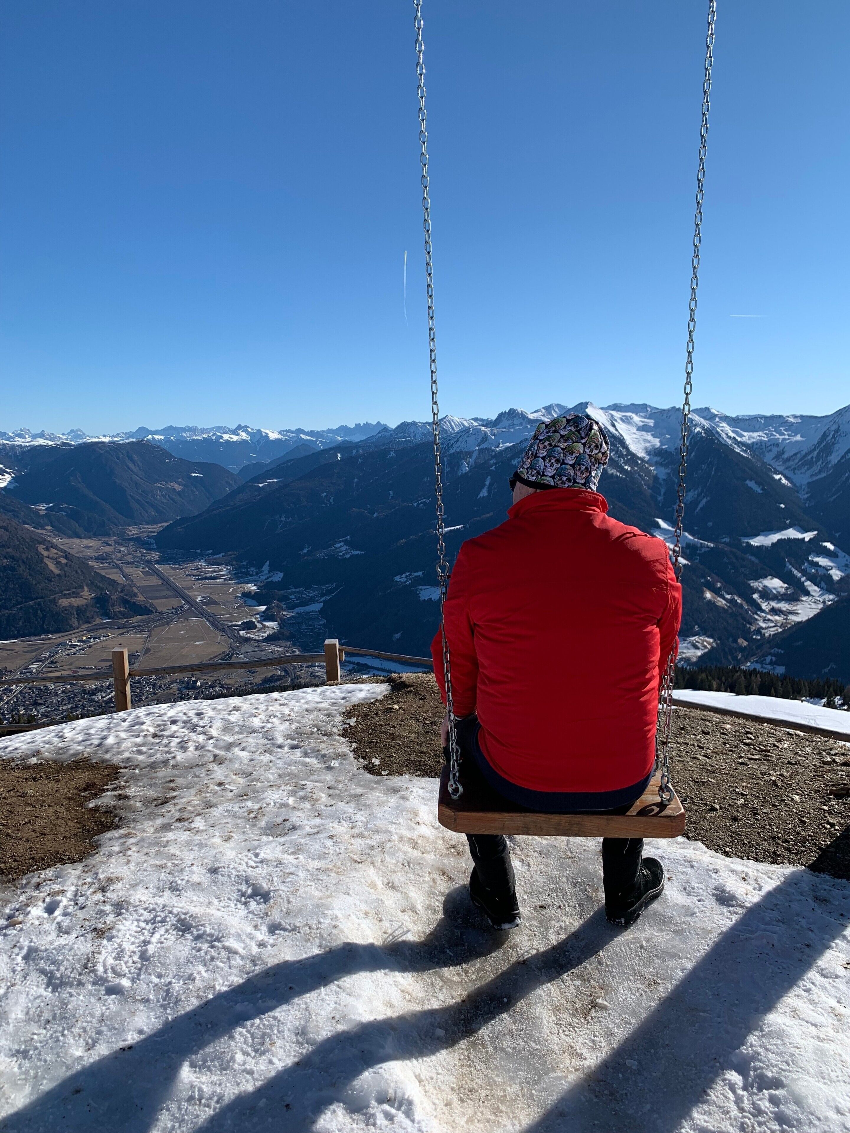 Une personne assise sur une balançoire, d’où elle peut admirer un paysage montagneux.