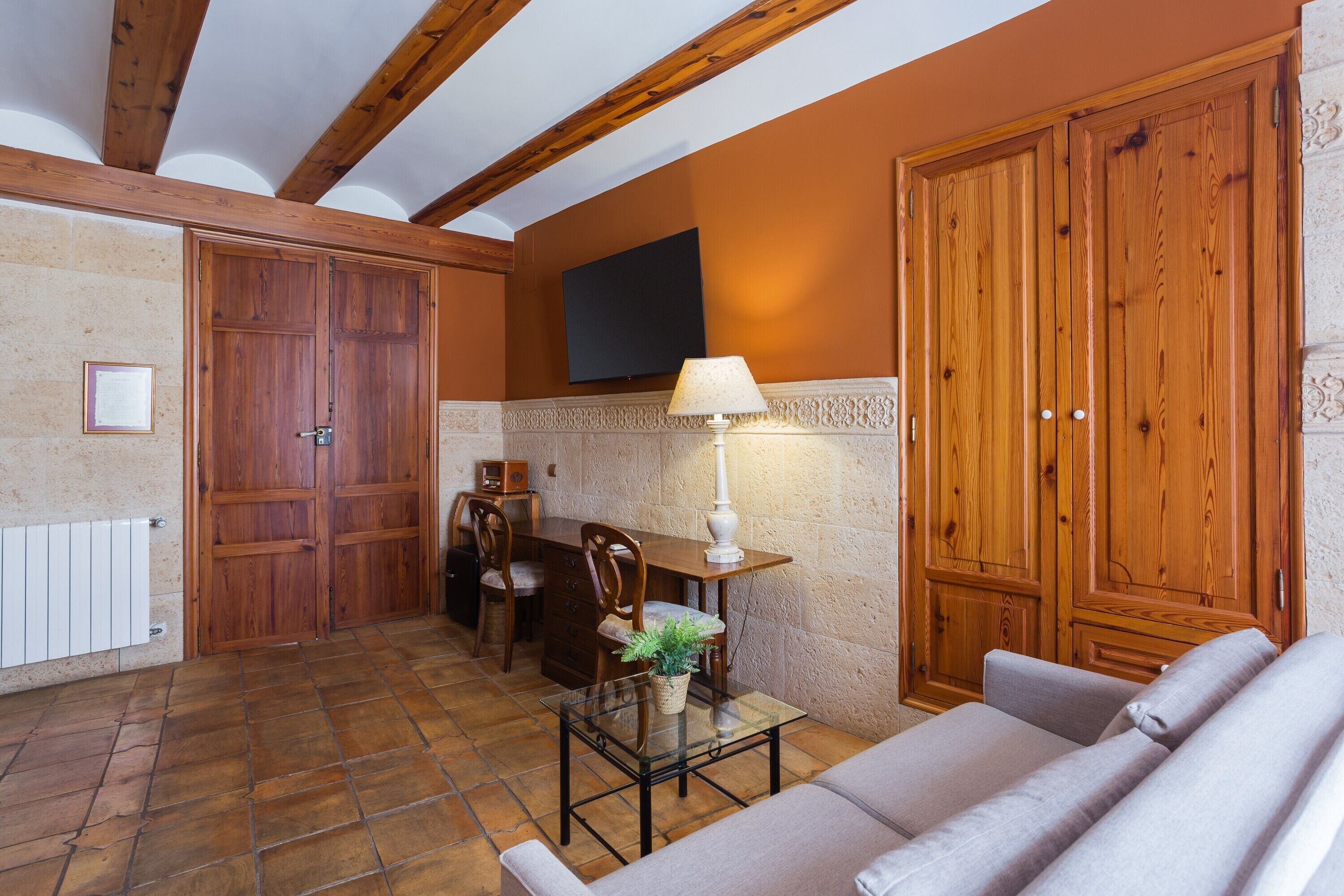 Une pièce avec un plafond en bois, un canapé, une table avec une lampe, un téléviseur et des portes en bois.