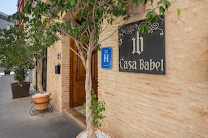 Un bâtiment sur lequel on peut lire l’inscription « Casa Babel », avec un arbre en pot et une enseigne bleue sur laquelle on distingue les lettres « H » et le mot « Superhotele ».