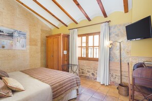 Une chambre à coucher avec un lit, une armoire en bois, un mur en pierre, une fenêtre avec des rideaux et un téléviseur fixé au mur.