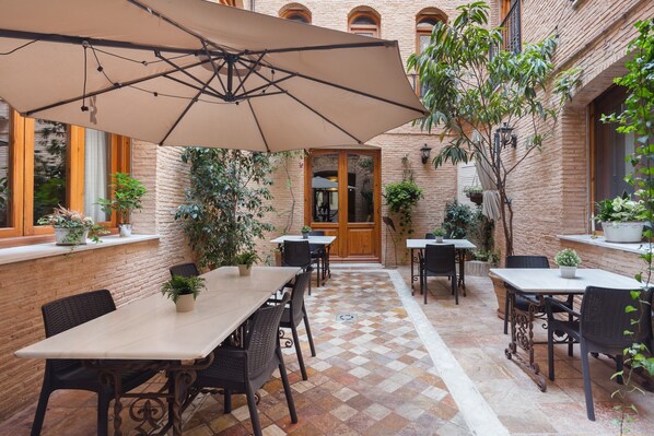Un espace extérieur aménagé en terrasse, avec des tables et des chaises, un grand parasol et des plantes en pot.