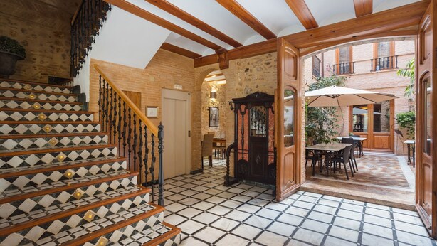 A staircase with patterned tiles, wooden beams, and a view of an outdoor patio area with tables and chairs. - Apartment 'Habitacion Estandar - Edificio Contiguo' with Private Terrace, Wi-Fi and Air Conditioning (Vilallonga)