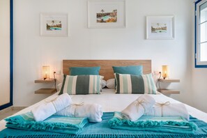 A neatly made bed with towels and a blue blanket, two bedside tables with lamps, and framed pictures on the wall.